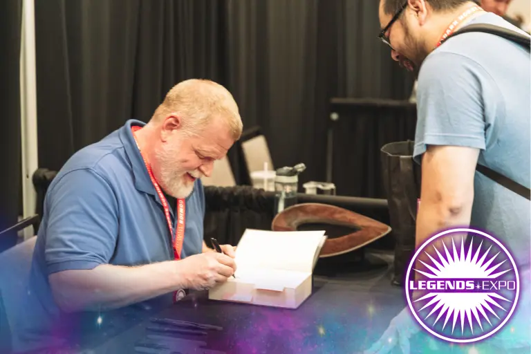 Author Matthew Stover smiles as he signs a book for a fan.