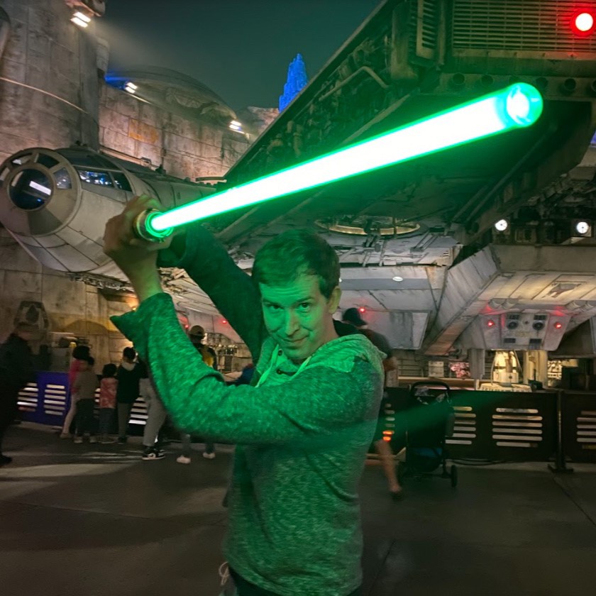 Charles Charles weilding a lightsaber outside the Falcon at Galaxy's Edge.